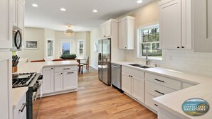 Une cuisine moderne avec des meubles blancs, un réfrigérateur en acier inoxydable et un plancher en bois.