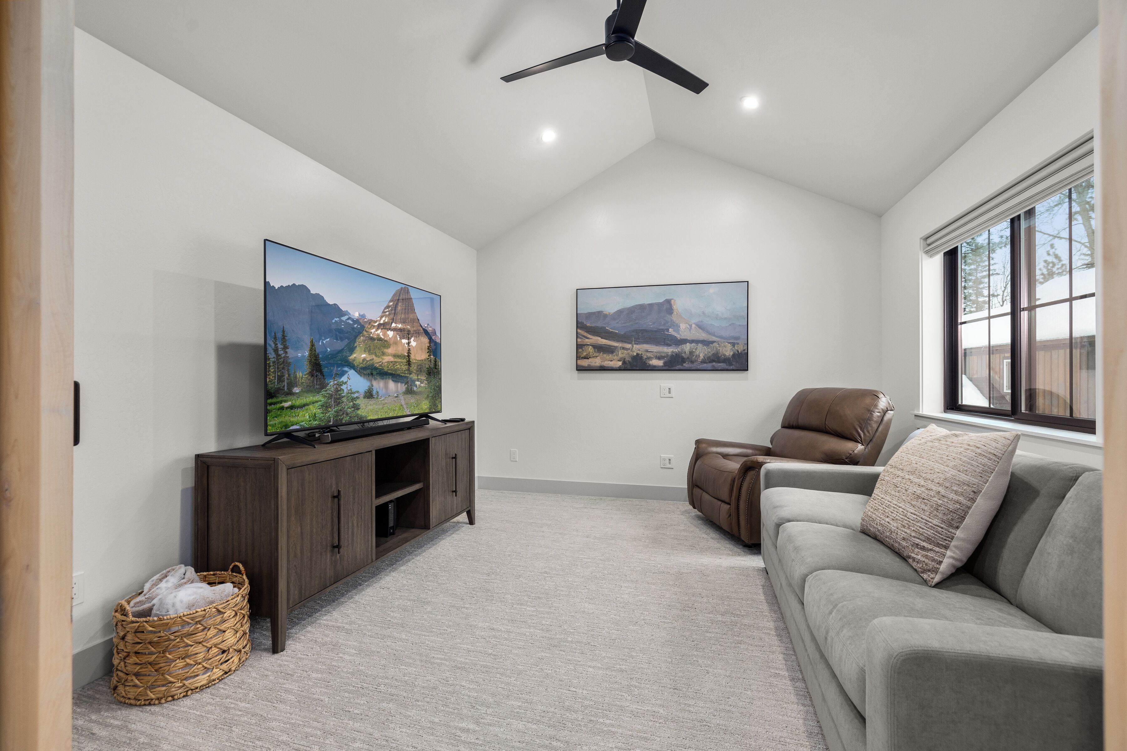 Una sala de estar con un televisor de pantalla plana, un sofá de cuero marrón, un sillón de cuero marrón y un ventilador de techo.