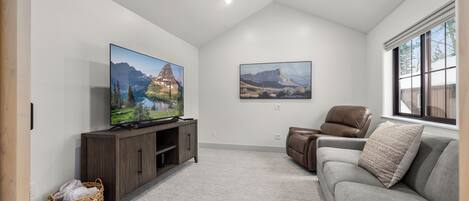 Una sala de estar con un televisor de pantalla plana, un sofá de cuero marrón, un sillón de cuero marrón y un ventilador de techo.