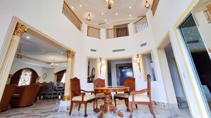 A spacious, elegantly furnished room with a high ceiling, ornate chandeliers, and a marble floor.