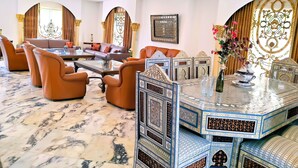 A luxurious living room with a marble floor, leather sofas, a glass coffee table, and ornate wall decorations.