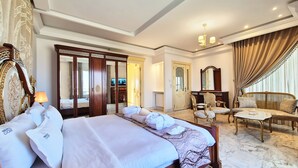 A spacious hotel room with a large bed, a sitting area with a sofa and chairs, a vanity with a mirror, and a television.