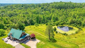 A lodge with a green roof, surrounded by lush greenery and a pond.