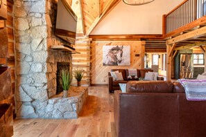 A rustic interior with a stone fireplace, wooden beams, a brown leather sofa, and a large painting on the wall.