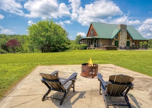 Eine Lodge mit einem Steinkamin, einer Feuerstelle und zwei Adirondack-Stühlen auf einer Beton-Terrasse.