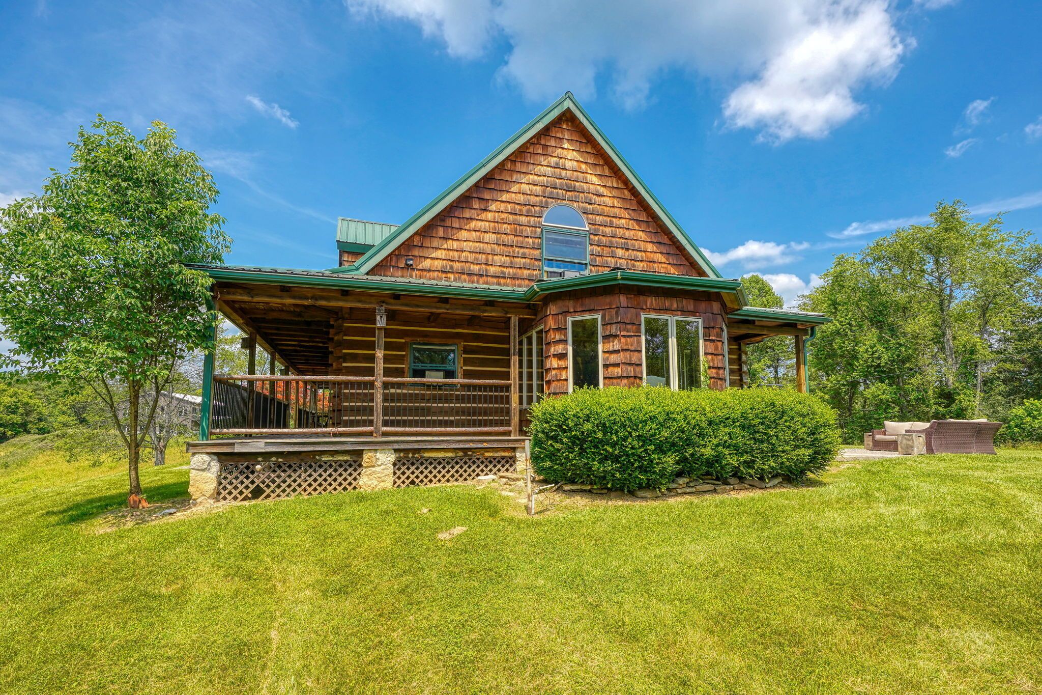 A log cabin with a porch, surrounded by a well-maintained lawn and trees.