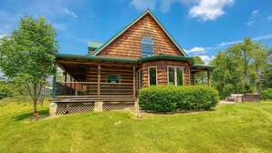 A log cabin with a porch, surrounded by a well-maintained lawn and trees. - Hidden Falls Lodge | Hocking Hills, 93 Acres (New Straitsville)