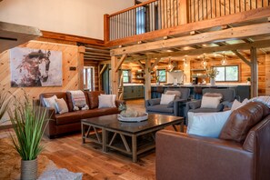 A spacious living area with a wooden ceiling, a dining table, and a kitchen in the background.