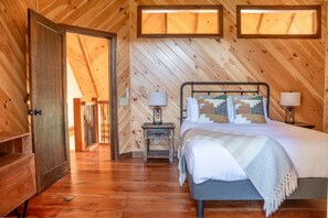 A wooden-paneled room with a bed, two bedside lamps, and a small table with a lamp.