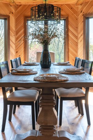 Una mesa de madera para comer con seis sillas, un jarrón grande con flores y una lámpara colgante.