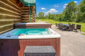 A hot tub with a wooden deck and a table with chairs outside a log cabin.