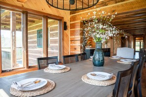 A wooden dining area with a large table set for four, surrounded by chairs, and a vase with flowers on the table.
