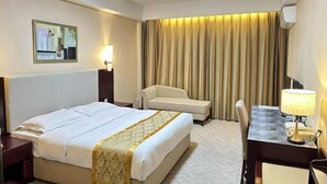 Ein Hotelzimmer mit einem Bett, einem Schreibtisch mit Lampe, einem Sessel, einer Couch und einem großen Fenster mit Vorhängen.