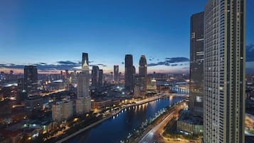 A cityscape at dusk with high-rise buildings, a river, and a bridge.