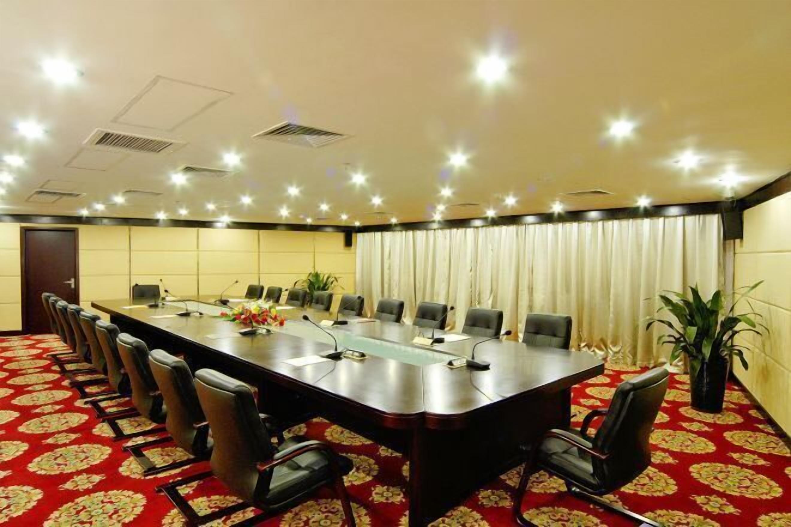 Un salón de conferencias con una larga mesa, varias sillas, micrófonos y una alfombra roja estampada.
