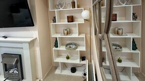 Een moderne woonkamer met een flatscreen-televisie, witte inbouwkasten, decoratieve objecten en een open haard.