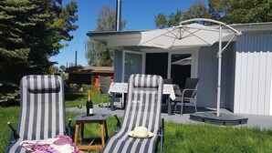 A patio area with two striped lounge chairs, a small table with a bottle and glasses, and a covered seating area with a table and chairs. - Haus Wellenrauschen - The vacation home "Wellenrauschen" the perfect place for peace and quiet (Zingst)