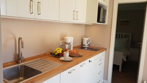 A compact kitchen with white cabinets, a wooden countertop, a stainless steel sink, a coffee maker, a kettle, and a breakfast setup including bananas and bread. - Haus Wellenrauschen - The vacation home "Wellenrauschen" the perfect place for peace and quiet (Zingst)