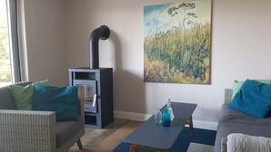 A living room with a sofa, a table, a painting, and a wood-burning stove. - Haus Wellenrauschen - The vacation home "Wellenrauschen" the perfect place for peace and quiet (Zingst)