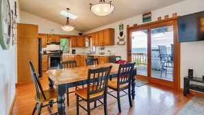 A kitchen with wooden cabinets, a dining table with chairs, and a view of the outdoors through a sliding glass door. - Sunrise Shores: Spectacular View! (Penn Yan)