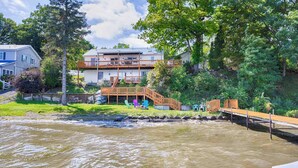 A two-story house with a wooden deck and a small staircase leading to the upper level. - Sunrise Shores: Spectacular View! (Penn Yan)
