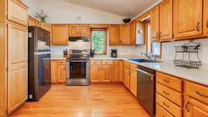 A kitchen with wooden cabinets, a stainless steel refrigerator, a dishwasher, and a double sink. - Sunrise Shores: Spectacular View! (Penn Yan)