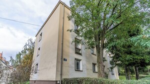 A multi-story building with a beige facade, a visible window, and a small garden area with a pathway. - Koszutka Blue Apartment (Katowice)