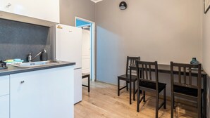 A compact kitchen with white cabinets, a built-in sink, and a refrigerator. There is a dining area with a wooden table and chairs. - Koszutka Blue Apartment (Katowice)