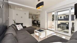Un salon moderne avec un canapé gris, une table basse et une grande porte-fenêtre coulissante donnant sur un espace de détente extérieur.