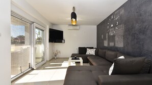 Un salon moderne avec un grand canapé d’angle, un téléviseur à écran plat fixé au mur et une horloge décorative.