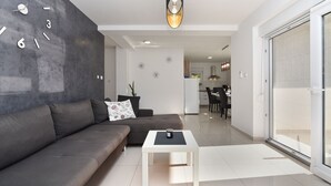 Un salon moderne avec un canapé gris, une petite table blanche et une grande fenêtre.