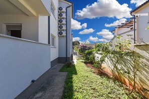 Stroll along the paved pathway to this modern residence, surrounded by a serene garden with lush plants and flowering shrubs.
