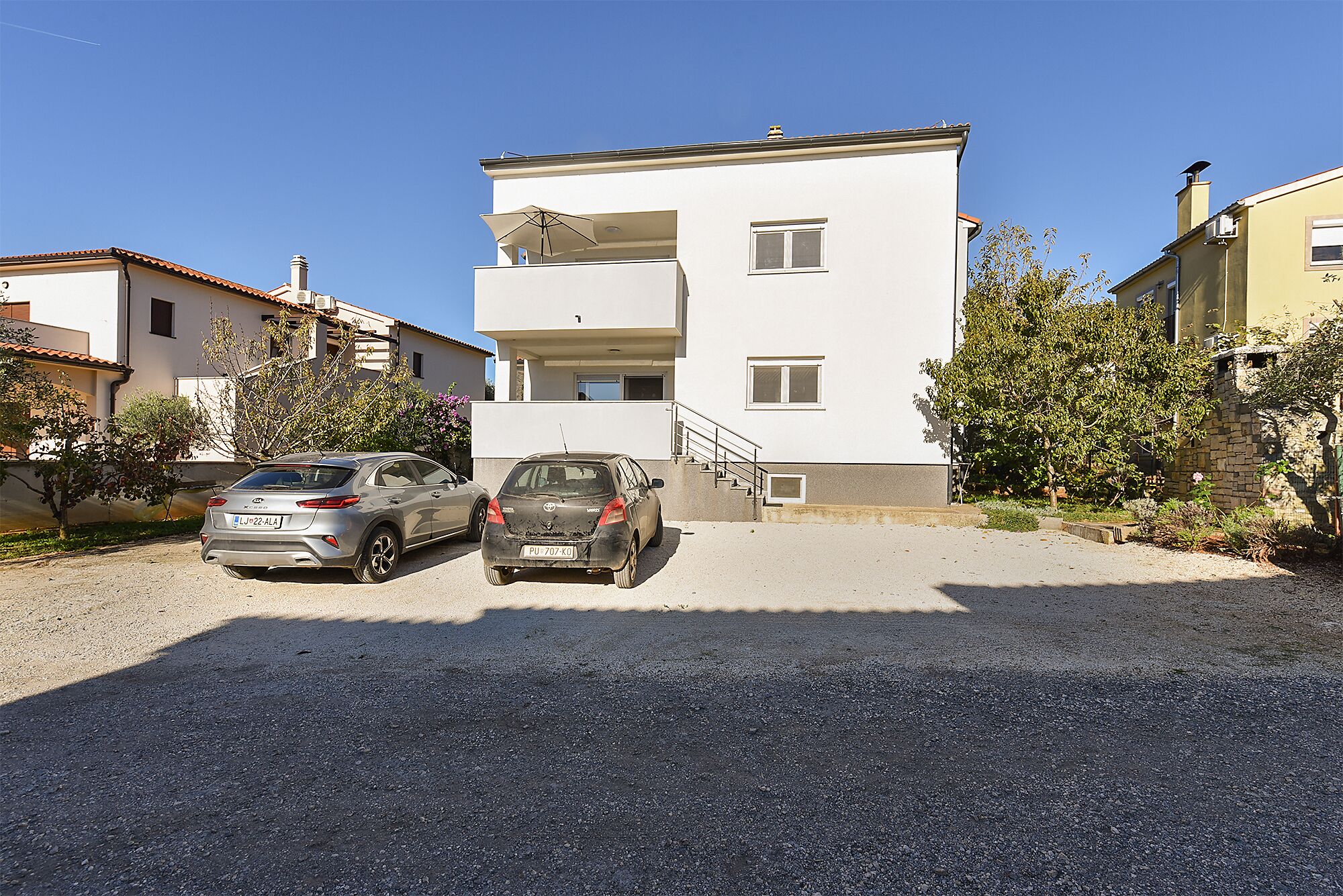 Un edificio residenziale a più piani con vialetto sterrato e due auto parcheggiate.