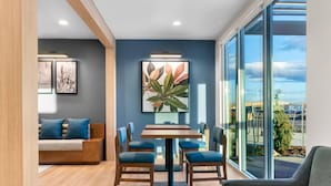 Un espace repas moderne avec une table en bois et des chaises recouvertes d’un tissu bleu, un canapé avec des coussins bleus et une grande fenêtre offrant une vue sur la ville.