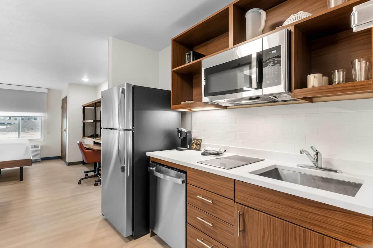 A modern kitchen with a stainless steel refrigerator, a microwave, and a dishwasher. There is a wooden countertop with a sink and a chair.