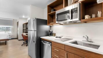 Cocina moderna con refrigerador de acero inoxidable, microondas y lavavajillas. Hay una encimera de madera con un lavamanos y una silla.