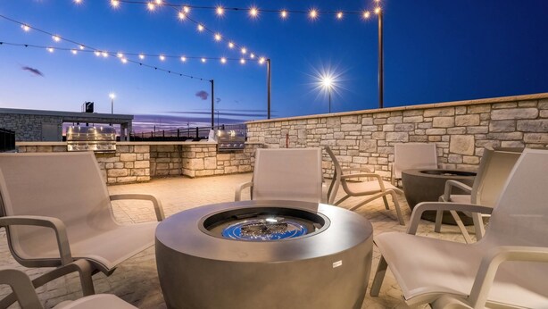 Une terrasse extérieure avec des murs en pierre, des guirlandes lumineuses, un foyer et des sièges d’extérieur.