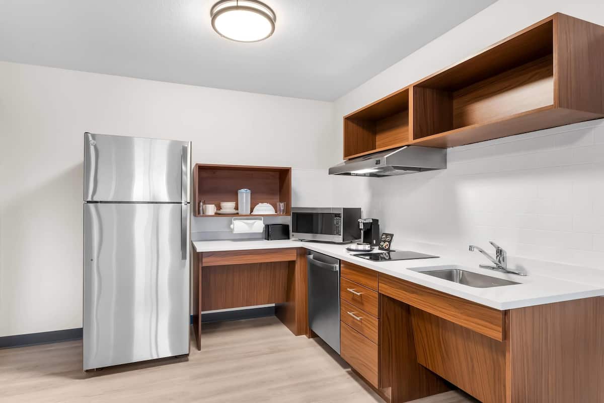A modern kitchen with a stainless steel refrigerator, a microwave, a coffee maker, and wooden cabinets.