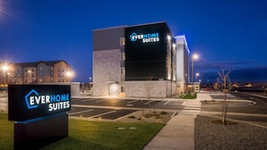 Un hôtel moderne avec une enseigne indiquant « EVERHOME SUITES » et un parking situé devant.