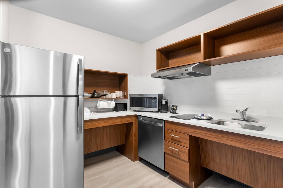 A modern kitchen with stainless steel appliances, wooden cabinets, and white countertops.