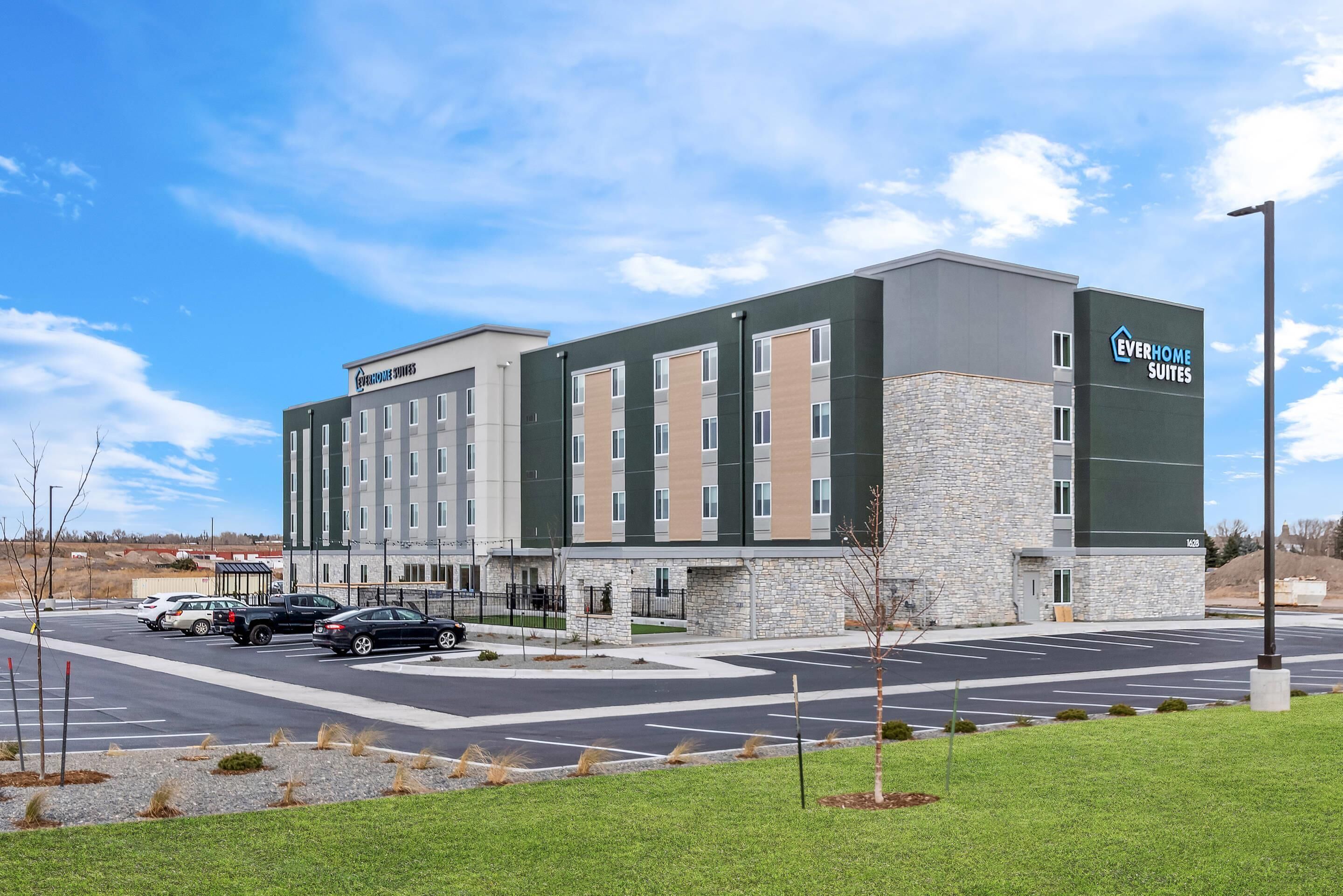 Un hôtel moderne à la façade en pierre, composé de plusieurs étages, doté d’un parking et offrant une vue sur un ciel dégagé.