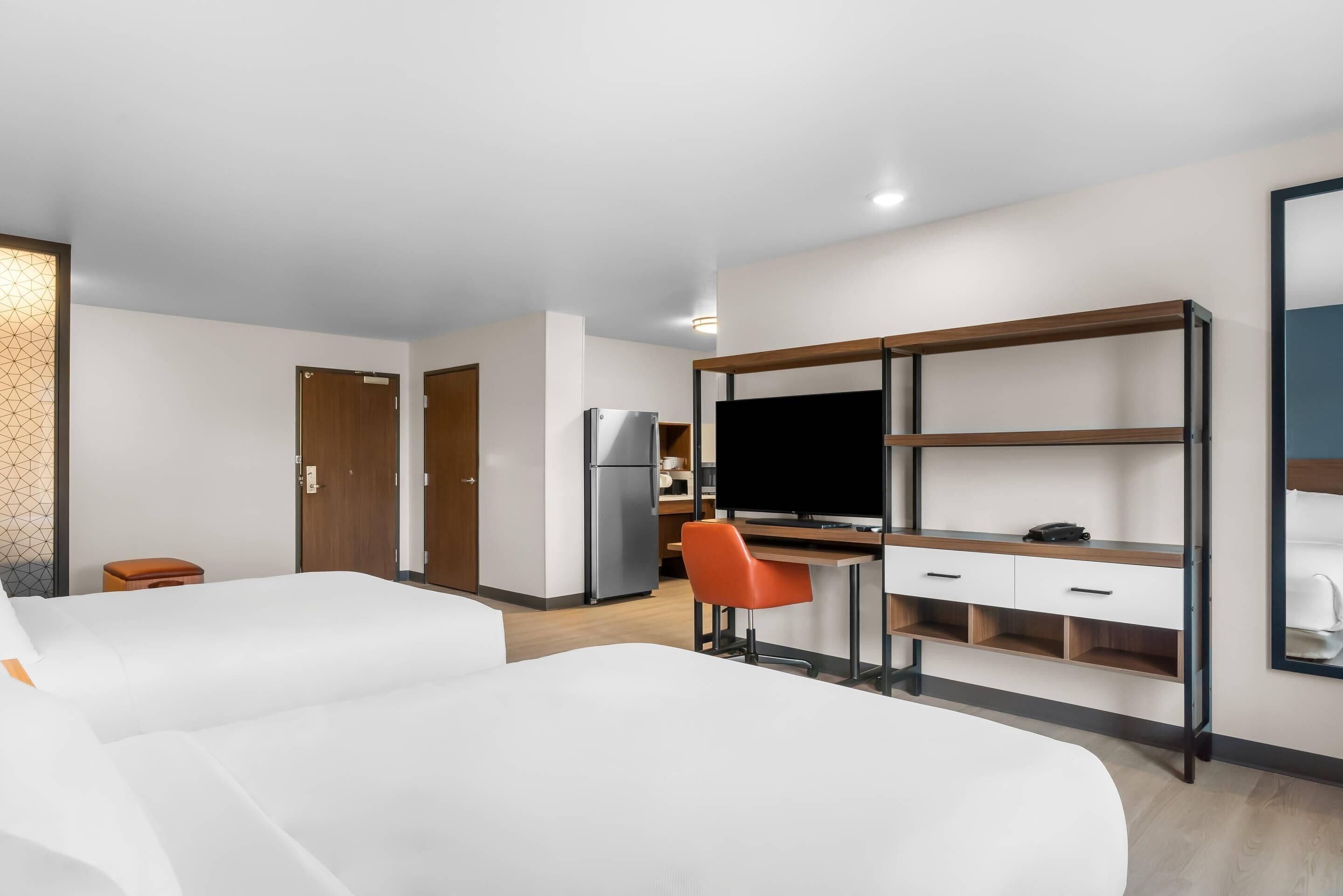 Une chambre d’hôtel avec deux lits, un bureau avec un ordinateur, une télévision et un réfrigérateur.