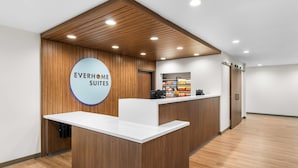 Un comptoir d’accueil avec une enseigne indiquant « EVERHOME SUITES », situé dans un intérieur moderne agrémenté de lambris en bois et d’un comptoir blanc.