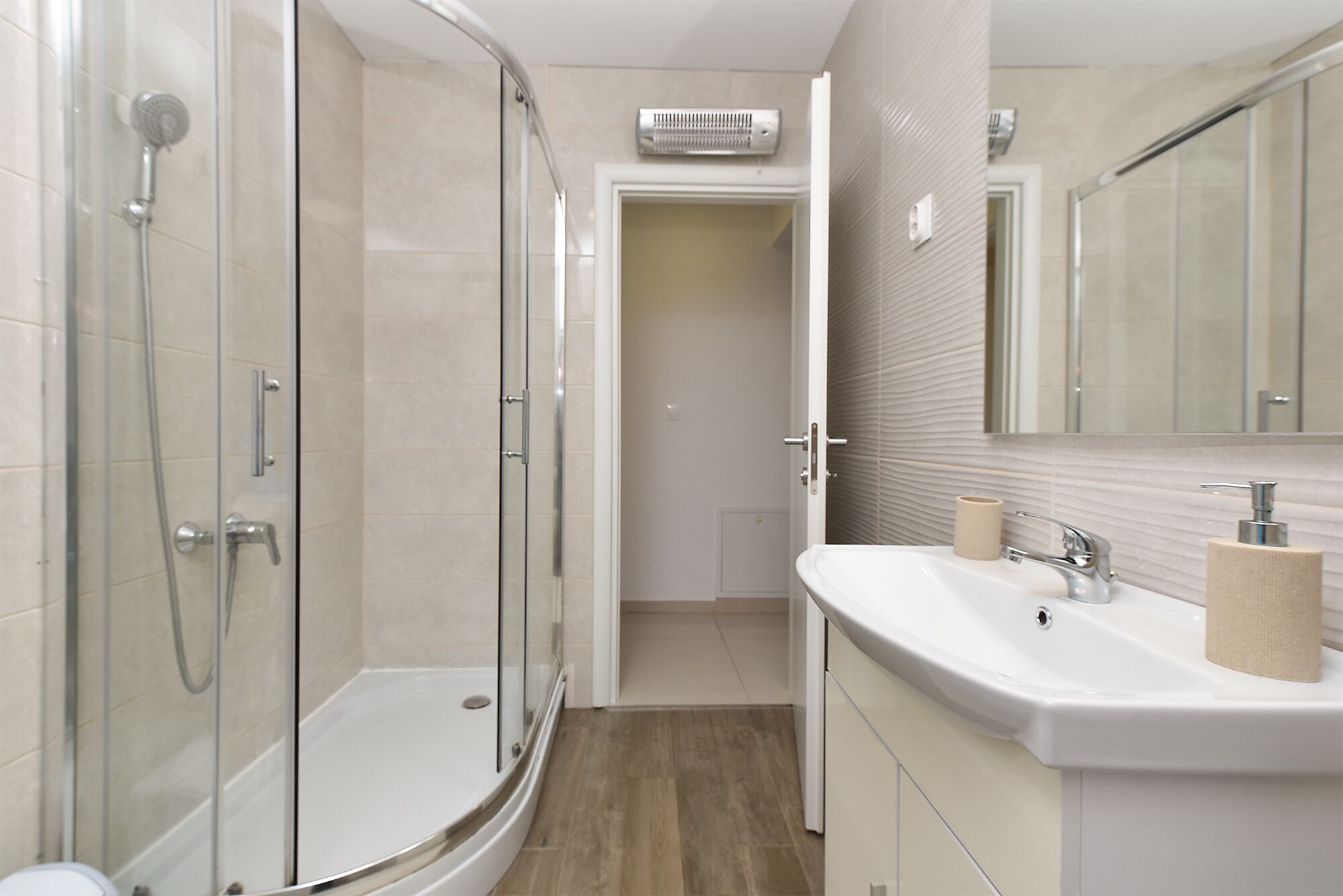 A modern bathroom with a glass-enclosed shower, a sink with a mirror, and a towel dispenser.