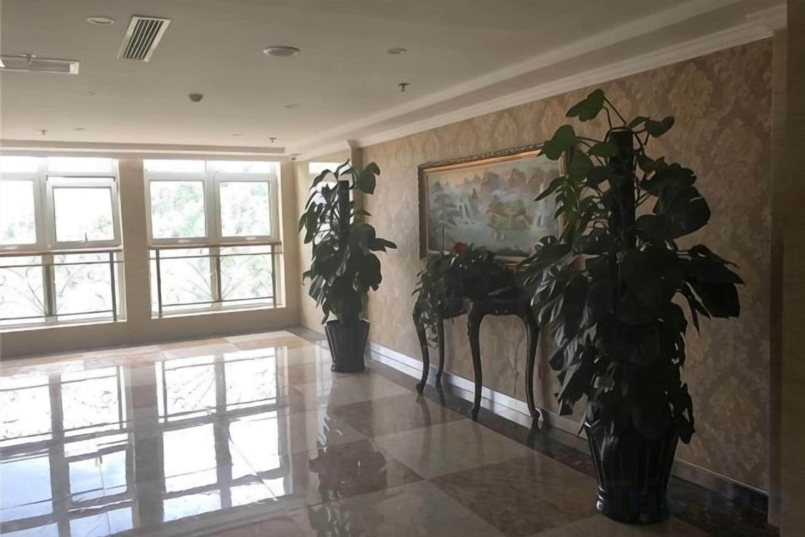 A spacious lobby with large windows, a polished floor, and several potted plants.