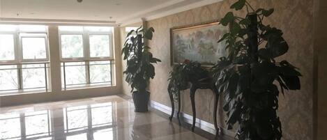A spacious lobby with large windows, a polished floor, and several potted plants.