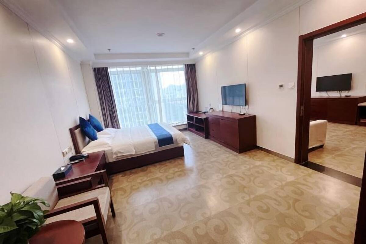 Ein Hotelzimmer mit Bett, Schreibtisch, Fernseher, Spiegel und einem großen Fenster.
