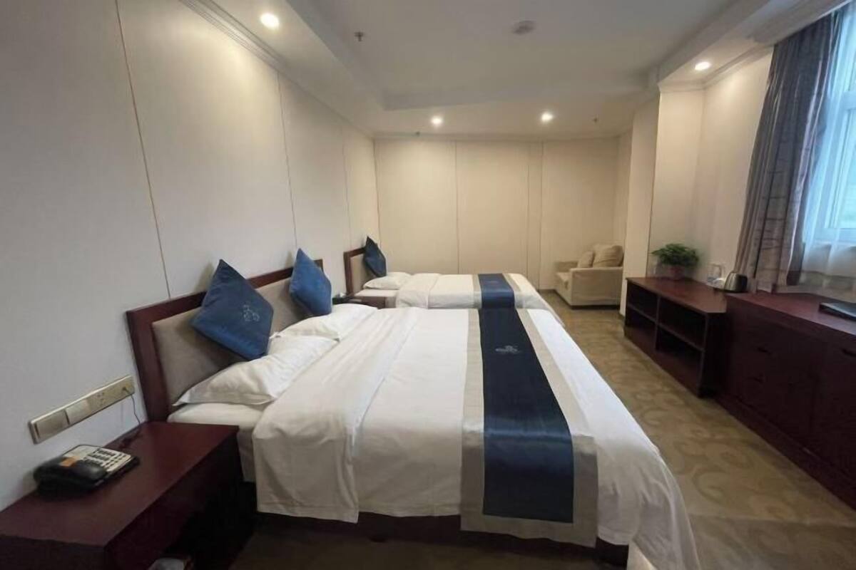 Ein Hotelzimmer mit zwei Betten, einem Schreibtisch, einem Stuhl, einem Fernseher und einem Fenster mit Vorhängen.