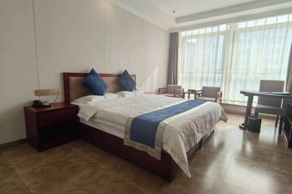 Ein Hotelzimmer mit Bett, Nachttisch, Stuhl und kleinem Schreibtisch mit Sitzmöglichkeit.