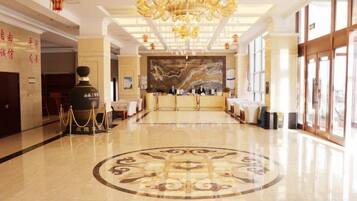 A hotel lobby with a reception desk, a chandelier, and a large window.